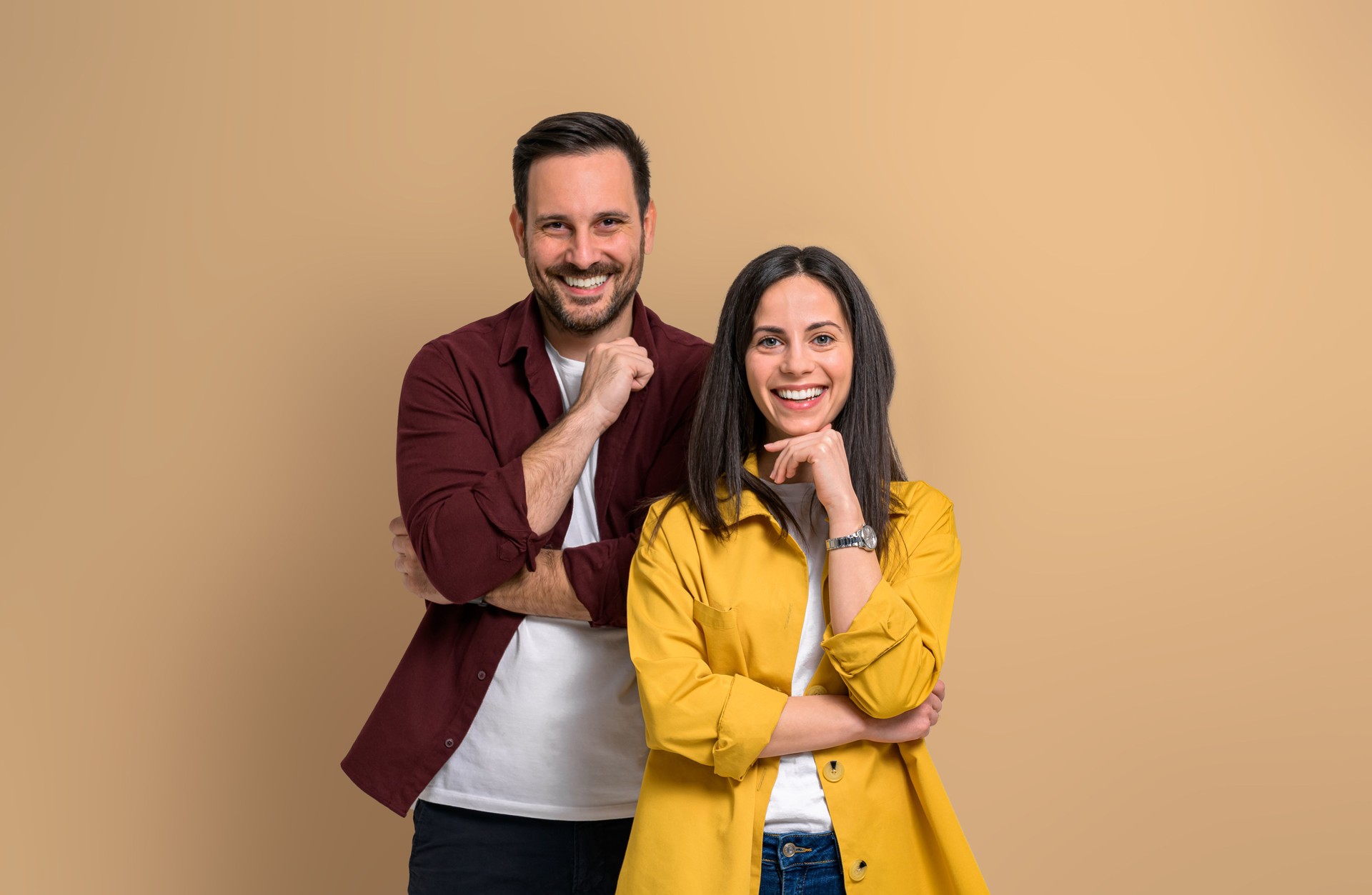 Charming young man and woman with hands on chins smiling and looking at camera. Confident joyful boyfriend and girlfriend wearing casuals and posing over beige background