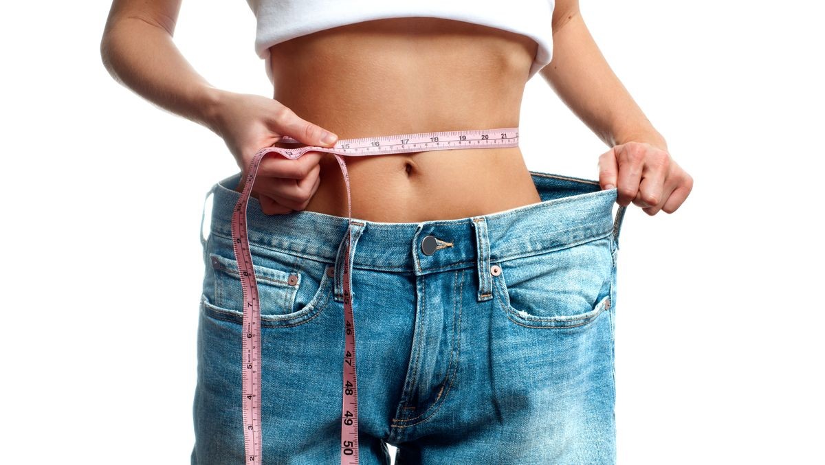 Woman is measuring waist after weight loss, diet concept. Woman in oversize jeans