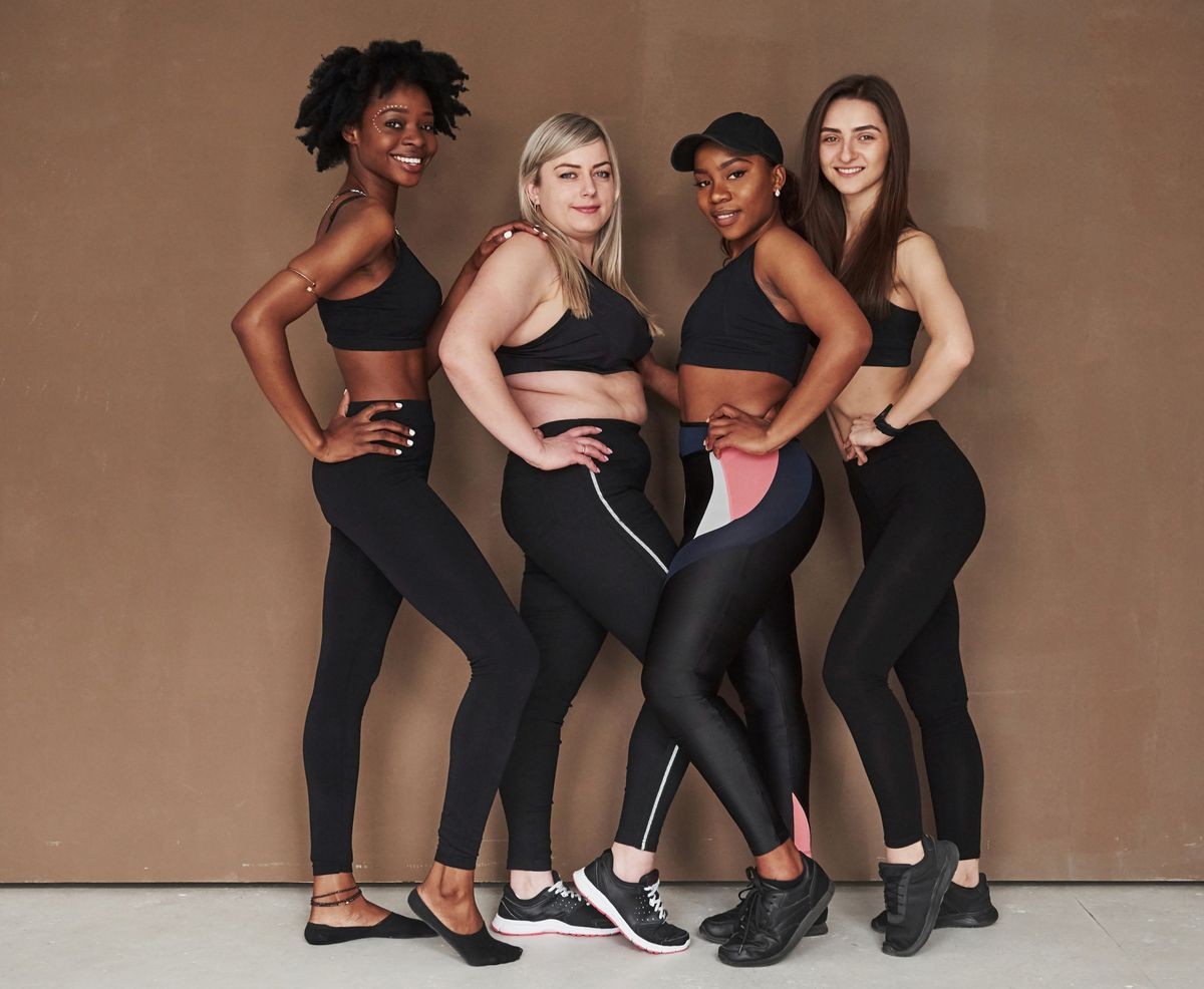 Full lenght photo. Group of multi ethnic women standing in the studio against brown background.